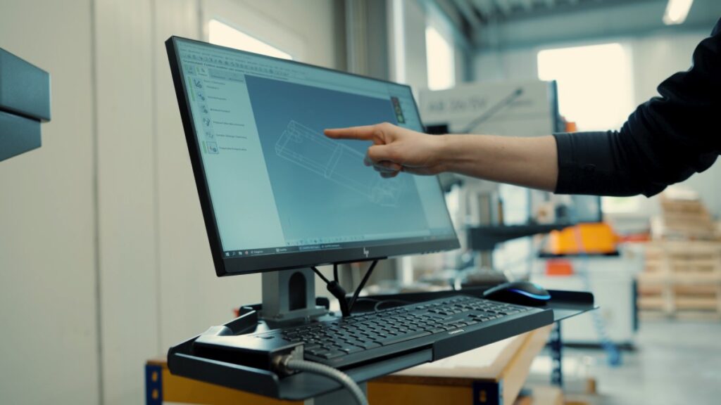 Hand zeigt auf die 3D-Ansicht eines Bauteils auf einem Monitor